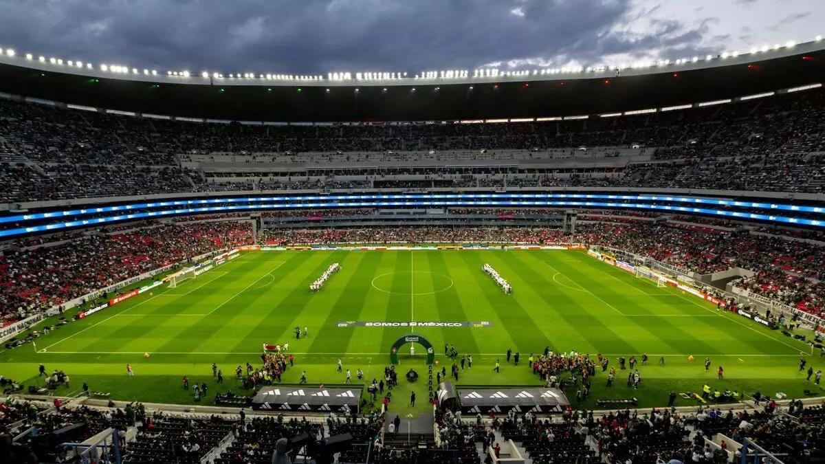 El Estadio Banorte de noche, con dos filas de jugadores de blanco en el centro de la cancha