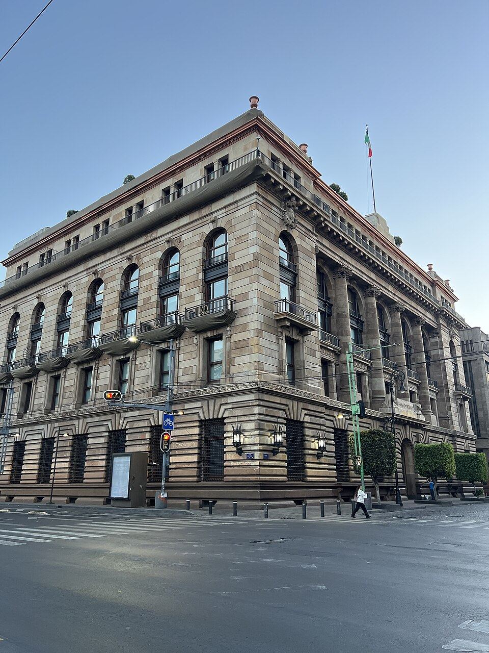 Peatones frente al Banco de México; tablero y fachada del instituto