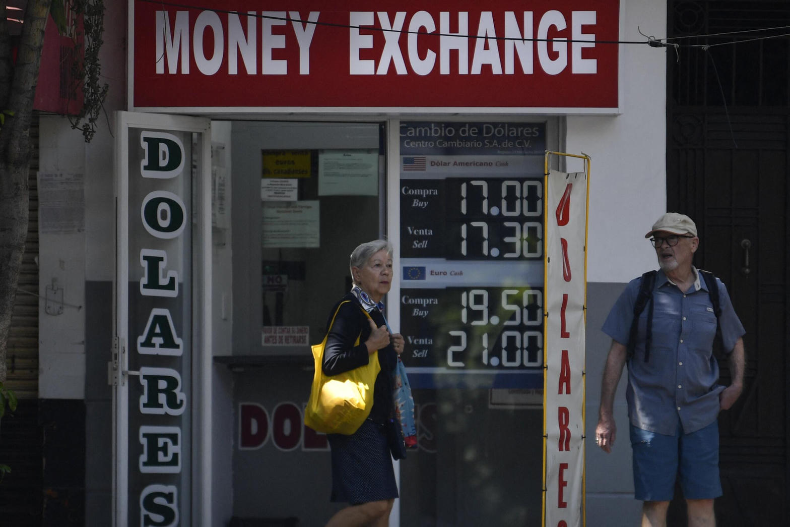 Peatones frente a una casa de cambio; tablero de compra y venta del dólar