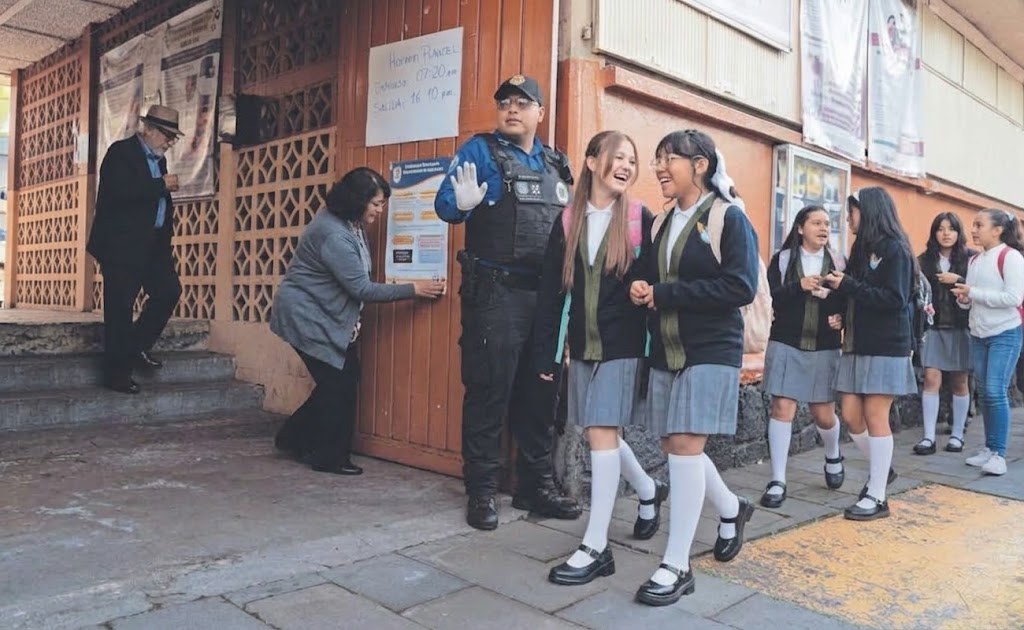 Estudiantes de secundaria con uniforme salen de la escuela; un policía alza la palma; una mujer pega un aviso en la puerta. A color