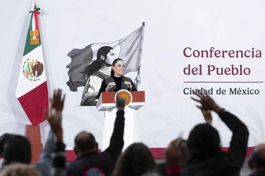 Claudia Sheinbaum, en escala de grises, en el podio de Tesorería; bandera, recinto y letrero Conferencia del Pueblo a color